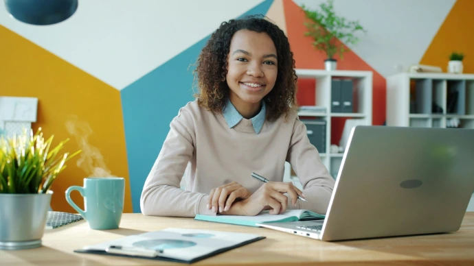 une dame qui sourit face caméro avec un ordinateur portable devant elle